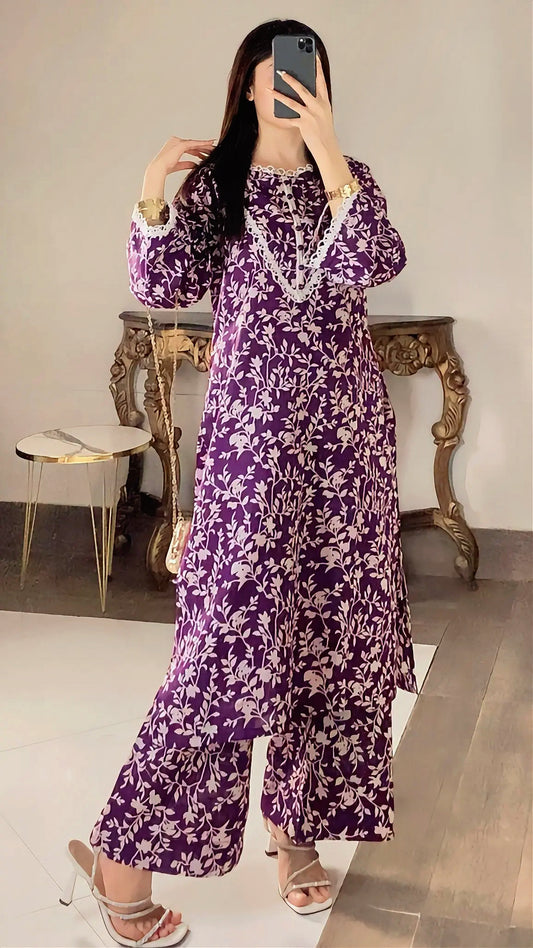 Person wearing a purple floral dress taking a mirror selfie in a room with a table and chair.