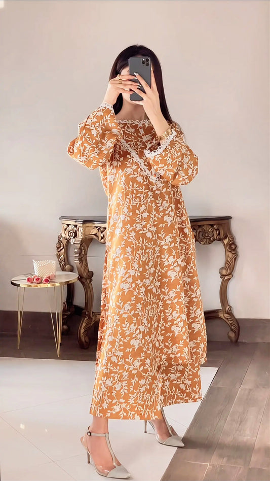 Woman taking a mirror selfie wearing an orange floral dress in a room with a table and chair.